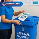 Person placing personal paper documents into lockable shredding bins for secure and confidential disposal.