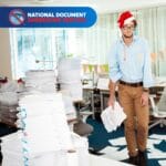 Man in Christmas hat buried in office paperwork ready to shred before Christmas with National Shred