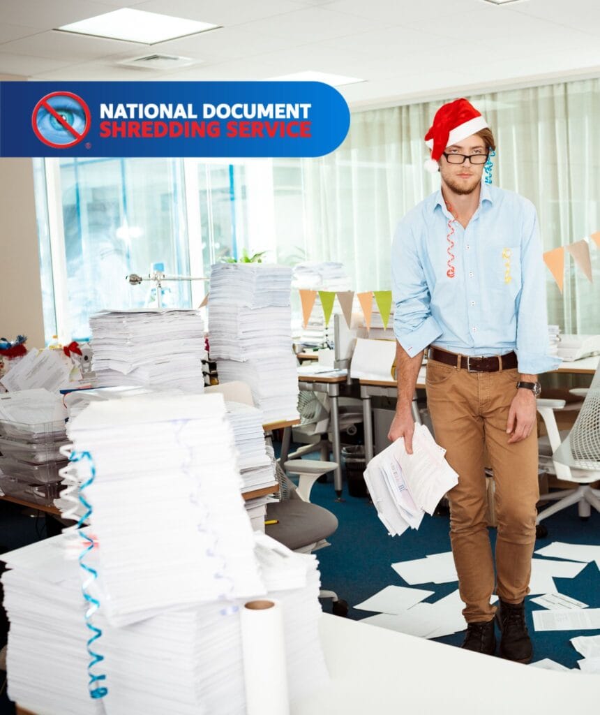 Man in Christmas hat buried in office paperwork ready to shred before Christmas with National Shred